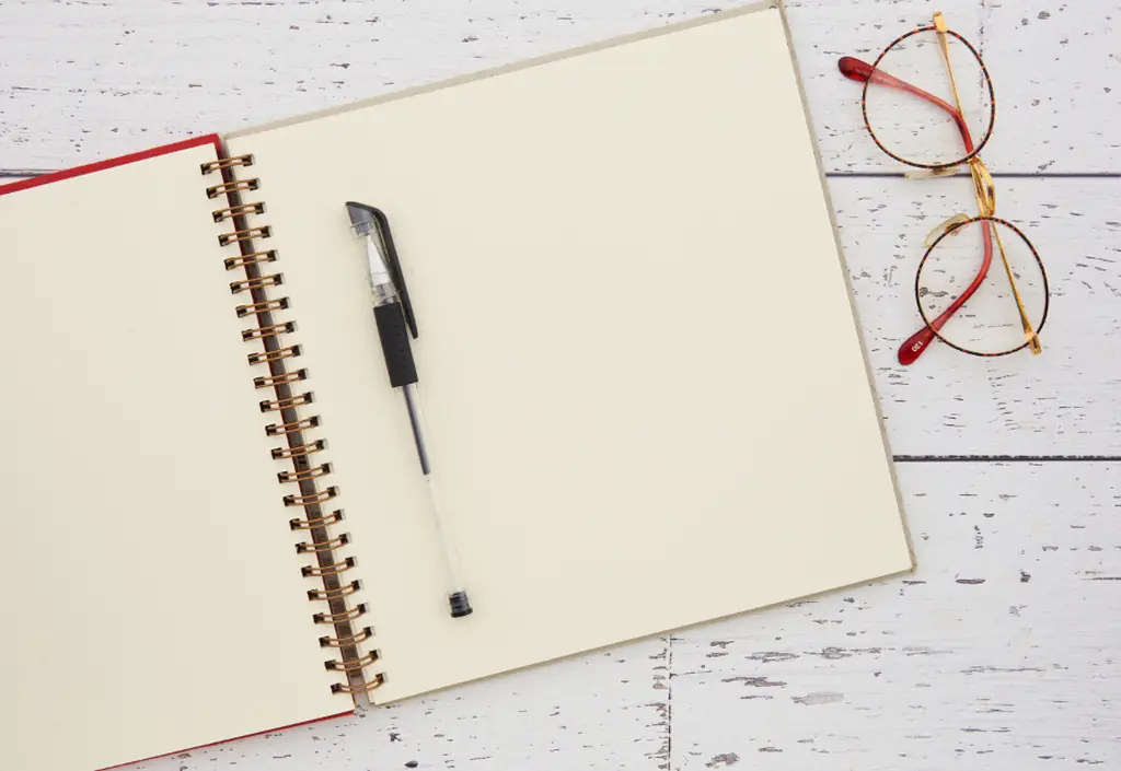 Lunettes, carnet ouvert et stylo reposant sur une surface blanche