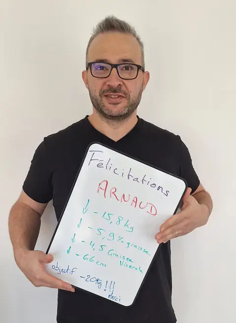 Un membre pose devant une ardoise blanche où sont notées ses mesures de bilan, au club